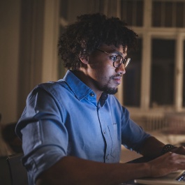 Young and determined black student studying at night at home, with a help of a laptop computer.