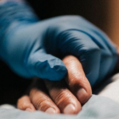 Someone with a medical glove on their hand, holding another person's hand.