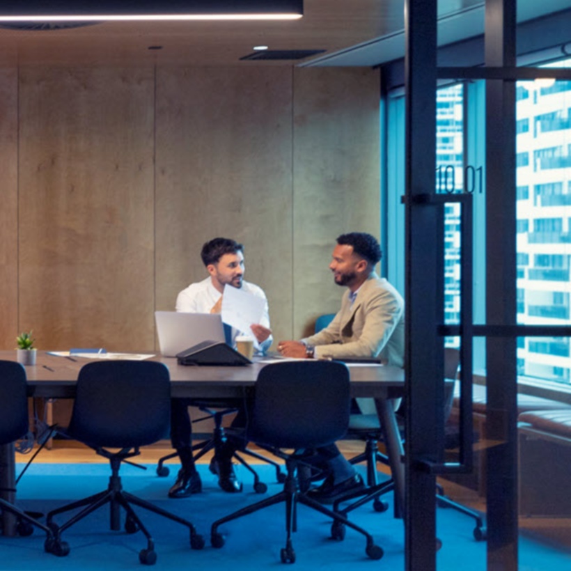 Two employees talking in a large board room style conference room.