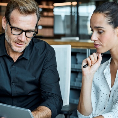 Two employees in an open office looking at a tablet. 