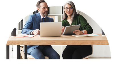 Co-workers sitting at a desk working together on their laptops.