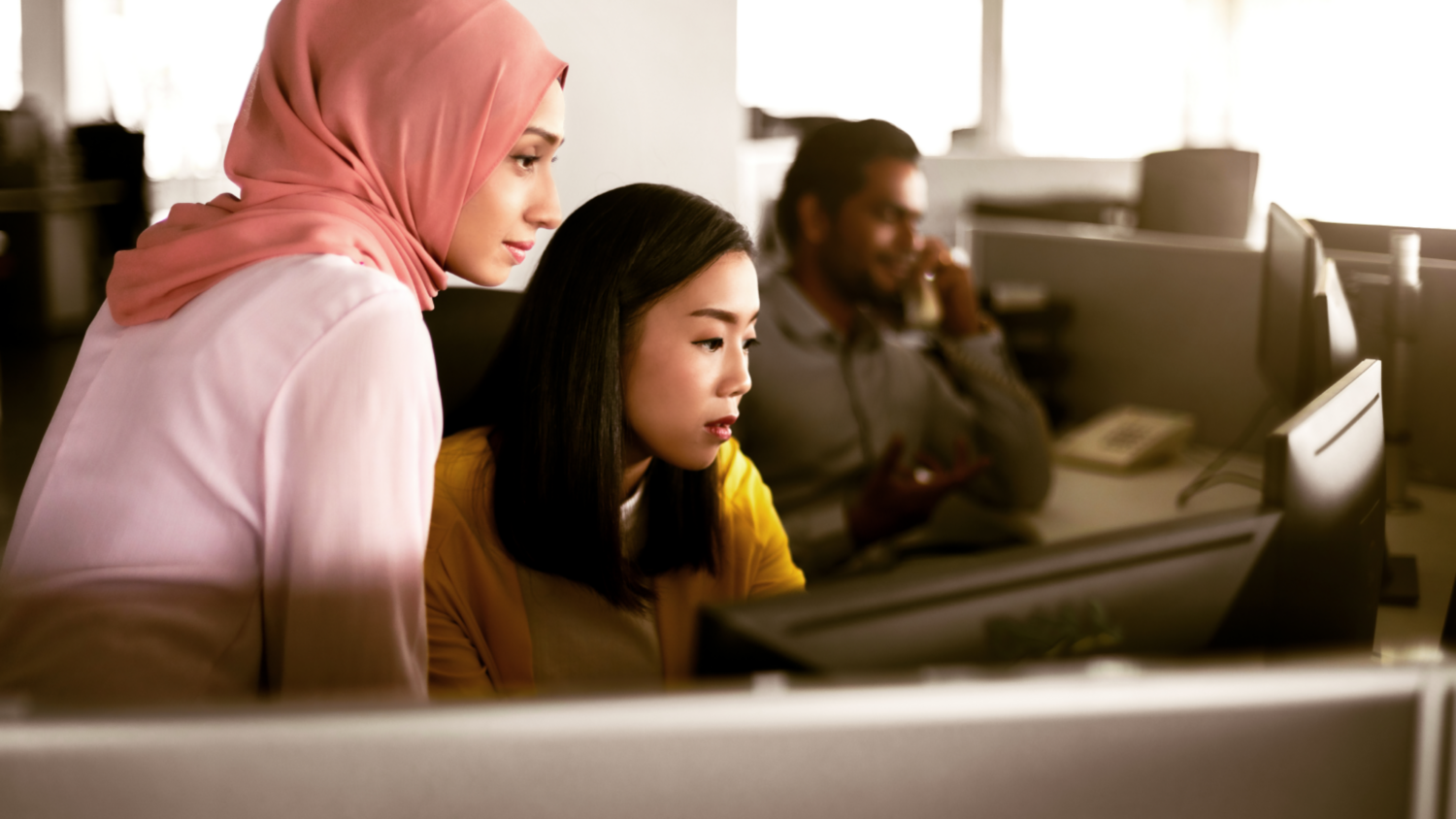 Two women looking at computer together in a cubicle