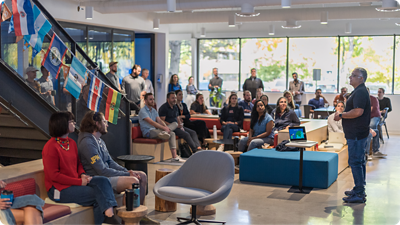 A group of employees sitting and listening to a standing employee, speaking to the group.