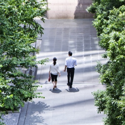 两个办公室工作人员走在人行道旁边绿色的树木