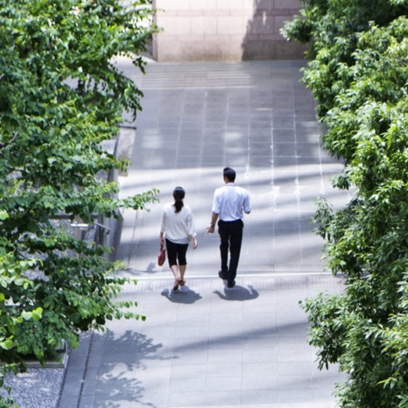 two office workers walking on sidewalk next to green trees