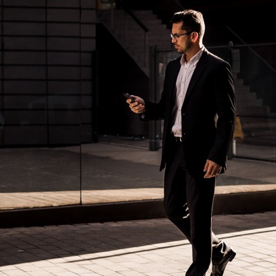 Man in a suit walking and talking on the phone in front of office buildings.