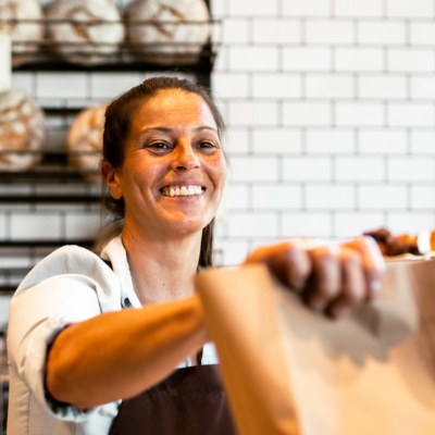 A woman working at a bakery serving a customer. 