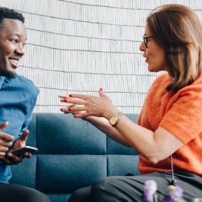 Two employees in conversation with each other while sitting on a couch