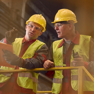 Two men in hi-vis jackets and protective gear having a conversation in a warehouse