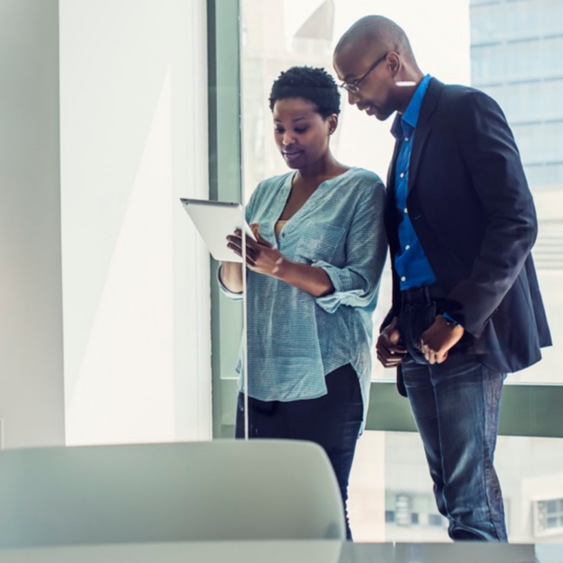 Two office workers looking at a tablet in a conference room