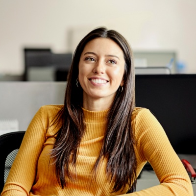 Woman in yellow shirt sitting in chair in cubicle smiling