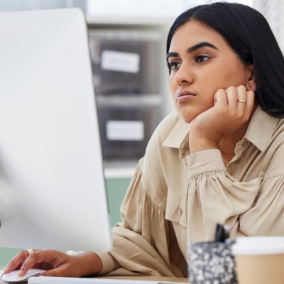 Unhappy employee sitting at a desk, looking at a computer